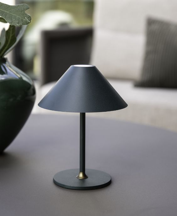 En modern, svart bordlampa på ett lågt bord utomhus i skymningen.