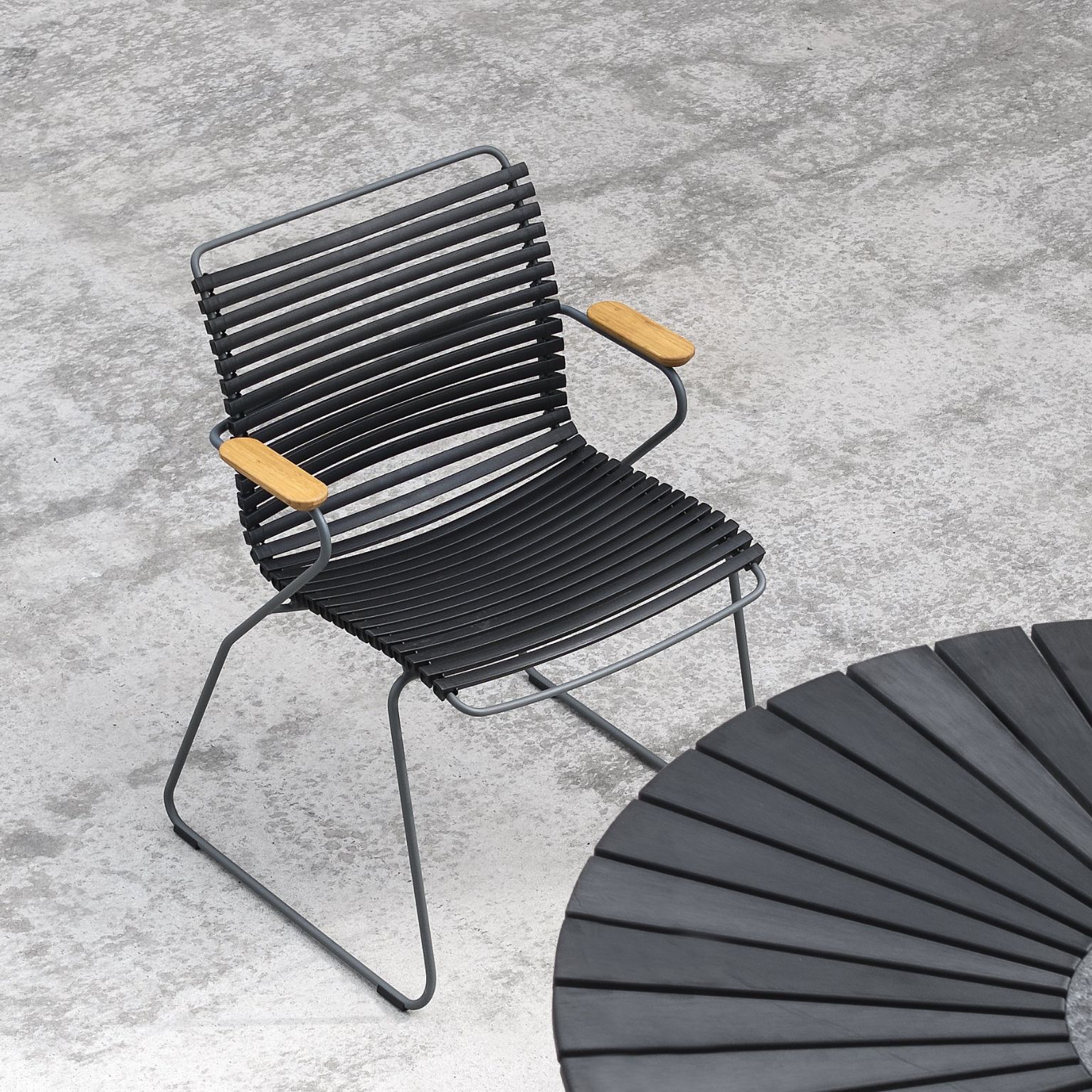 Enskild modern flätad stol med metallben och träarmstöd på en betongyta