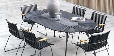 Modernt utomhus matområde med svarta flätade stolar och ett stort ovalt bord, dekorerat med en vas och en lykta på en betongterrass.