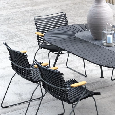 Modernt utomhus matområde med svarta flätade stolar och ett stort ovalt bord, dekorerat med en vas och en lykta på en betongterrass.