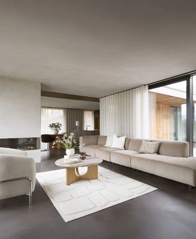 Lyxigt vardagsrum med en lång beige soffa, runda soffbord i trä och sten, omgiven av stora fönster med utsikt över naturen.