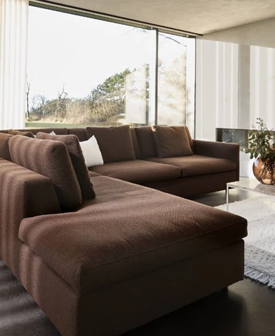 Modernt vardagsrum med mörkbrun hörnsoffa, stor golvlampa och öppna ytor med stora panoramafönster.