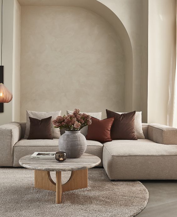 Mysig vardagsrumsinredning med beige hörnsoffa, runt träbord, dekorativa kuddar och en stilfull matta