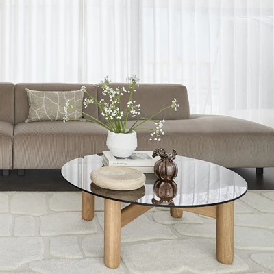 Ett vardagsrum med en mörkgrå soffa och ett runt soffbord i glas framför, där en vas med blommor och dekorativa element står