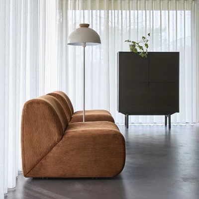 Två moderna fåtöljer i mörkorange står på ett betonggolv. Mellan dem står en vit golvlampa. Bakom finns en byrå i mörkt trä.