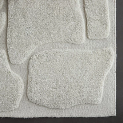 Detaljerad bild av en vit matta med organisk design i hög, lös vävning.