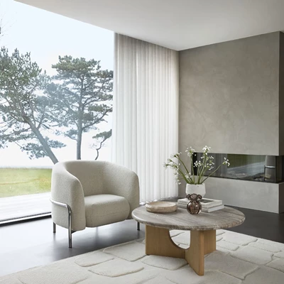 Mysigt hörn med en modern, vit fåtölj vid ett runt soffbord och ett stort fönster med utsikt över naturen.