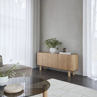 Sideboard i ljust trä med minimalistisk design och dekorationer som en växt och skulpturala objekt.