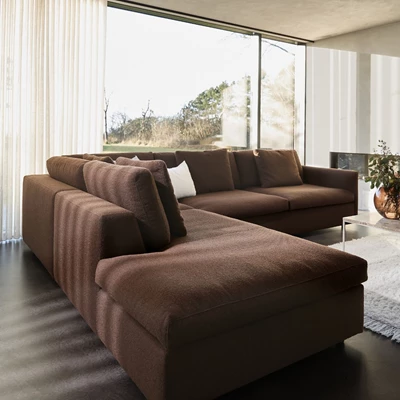 Perspektiv av mörkbrun modulsoffa sedd från sidan, med stort fönster och utsikt mot utomhusmiljön.