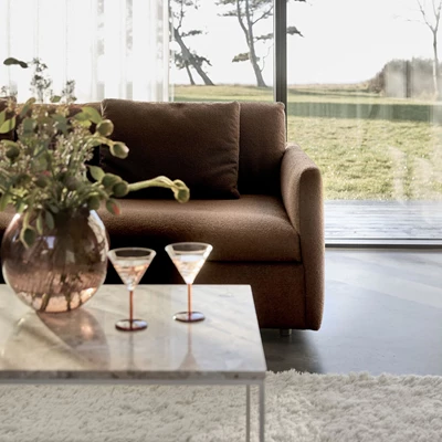 Mysigt hörn med mörkbrun soffa och ett soffbord i glas med martiniglas och vas.