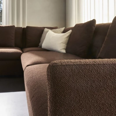 Närbild av en del av mörkbrun modulsoffa med en offwhite kudde, där det texturerade tyget syns tydligt.