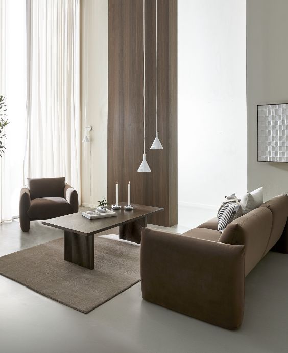 Modernt vardagsrumsinredning med två mörkbruna läderfåtöljer och ett rektangulärt lågt bord mellan dem. Bakgrunden visar långa, mörka träpaneler och en vit skulpturell väggdekoration.