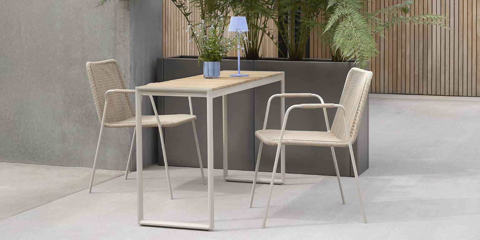 Enkel och stilren balkonginredning med ett litet bord och två flätade stolar under en minimalistisk lampa.