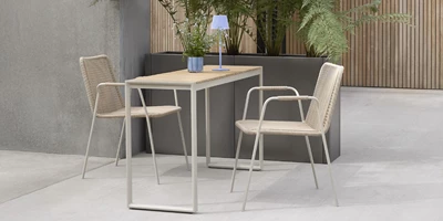 Corfu Enkel och stilren balkonginredning med ett litet bord och två flätade stolar under en minimalistisk lampa.