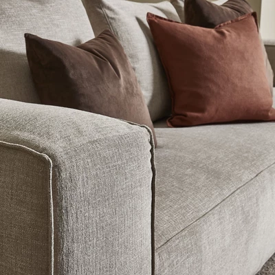 Närbild av en beige soffa med textur och kvalitetstyg, dekorerad med mörkröda sammetskuddar.