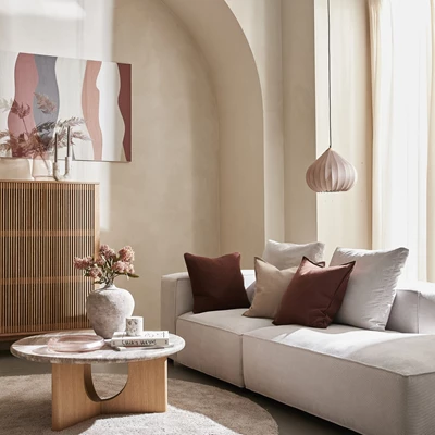 Elegant vardagsrum med beige soffa, soffbord i trä och en dekorativ pendellampa, stämningsfullt inrett med mjuka färger och modern konst.