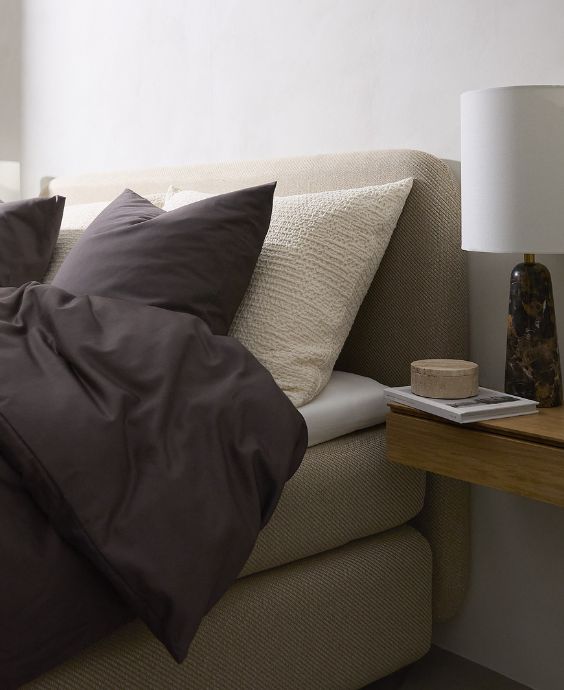 Mysigt hörn av sovrummet med höga sängändar och mörkt sängkläder, framhävt av mjukt, naturligt ljus.