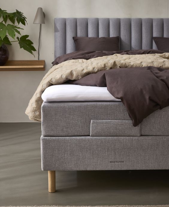 Elegant grå elevationssäng med högt huvudgavel och lager av mysigt, brunt och vitt sängkläder i ett modernt sovrum.