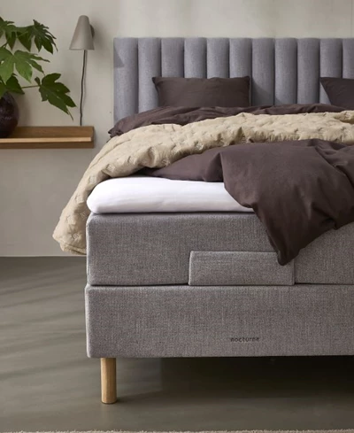 Elegant grå elevationssäng med högt huvudgavel och lager av mysigt, brunt och vitt sängkläder i ett modernt sovrum.