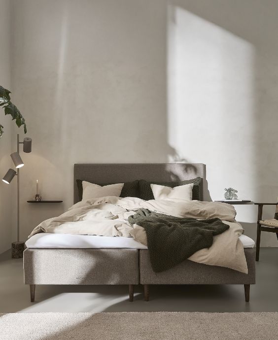 Minimalistiskt sovrum med en låg, modern säng med grått sängkläder och avslappnad atmosfär.