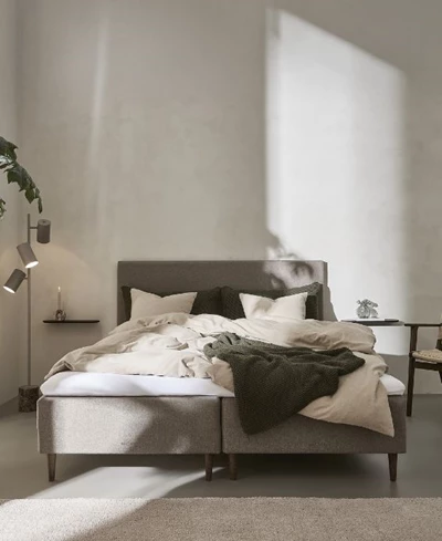 Minimalistiskt sovrum med en låg, modern säng med grått sängkläder och avslappnad atmosfär.