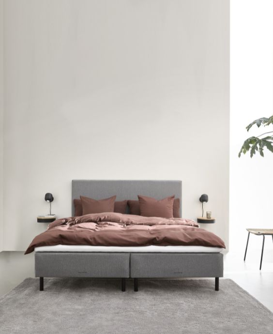 Modernt sovrum med en enkel ramsäng i brunt och beige färgtema och en krukväxt som dekoration.