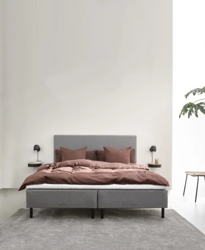 Modernt sovrum med en enkel ramsäng i brunt och beige färgtema och en krukväxt som dekoration.