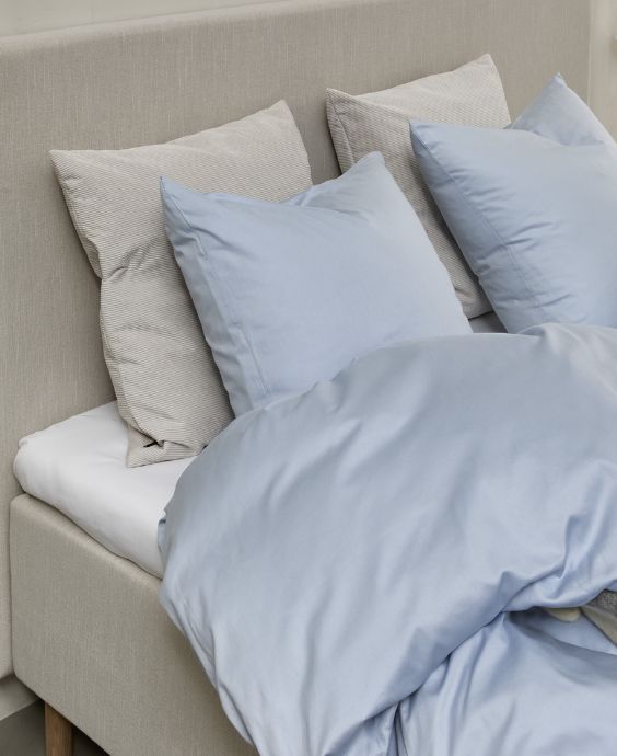 Ljusblått sängkläder på en elegant boxsäng i ett ljust sovrum med modern estetik och fridfull stämning.