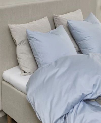Ljusblått sängkläder på en elegant boxsäng i ett ljust sovrum med modern estetik och fridfull stämning.