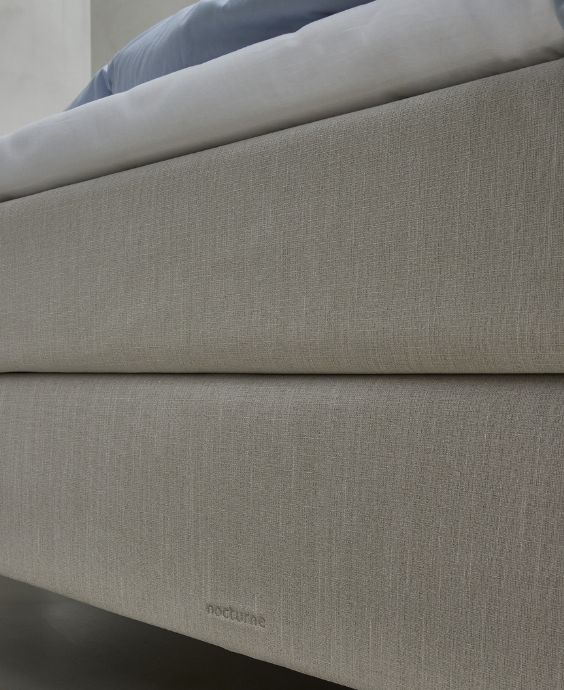 Närbild av en beige boxmadrass som visar texturernas detaljer och varumärket Nocturne broderat i tyget.