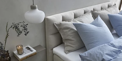 Design uden navn - 2025-03-13T142912.288.jpg Säng med ljus, horisontellt stoppad gavel, blåa sängkläder, levande ljus och liten vägghylla.