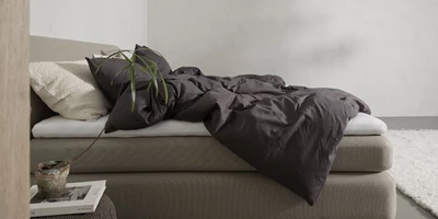 Design uden navn - 2025-03-16T195358.008.jpg Modernt sovrum med låg, stoppad säng och mörklila sängkläder, minimalistisk inredning.
