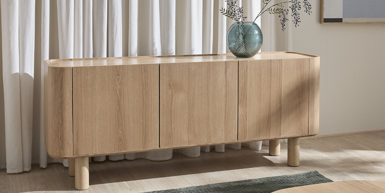 Träskänk framför gardiner med blå glasvas