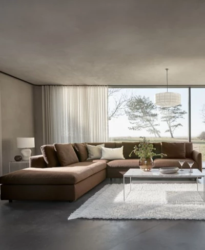 Stor brun hörnsoffa med puffavslutning placerad i ett minimalistiskt vardagsrum.