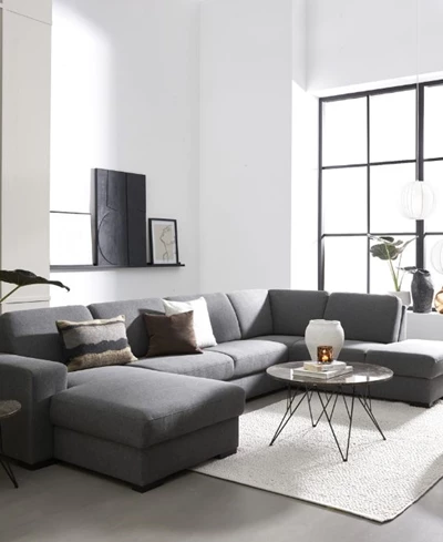 Klassisk grå soffa med puff och schäslong placerad i ett enkelt vardagsrum.