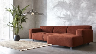 Röd schäslongsoffa placerad på betongolv.