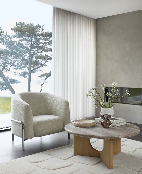 Vit stoppad fåtölj med kromstativ stående framför stort glasparti vid sidan av soffbordet