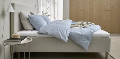 Boxspring i grått sedd från sidan med kudde och täcke i blått