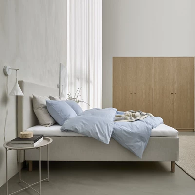 Boxspring i grått sedd från sidan med kudde och täcke i blått