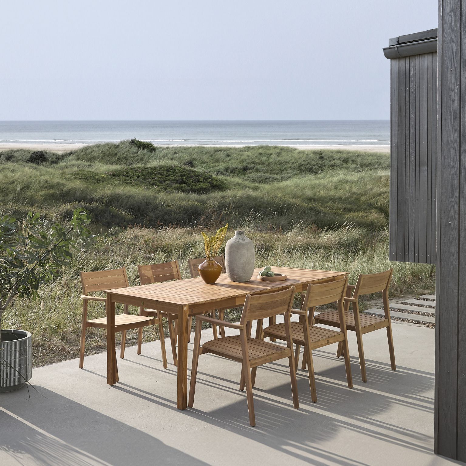 Trädgårdsbord med sex stolar i trä på en terrass.