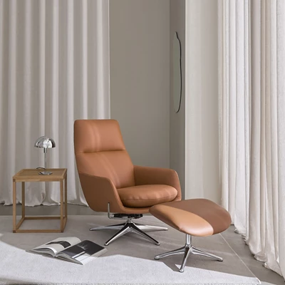 Fåtölj och fotpall i brunt läder tillsammans med ett sidobord i trä.