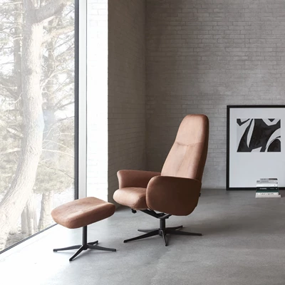 Fåtölj och fotpall i brunt läder stående i ett grått betongrum.