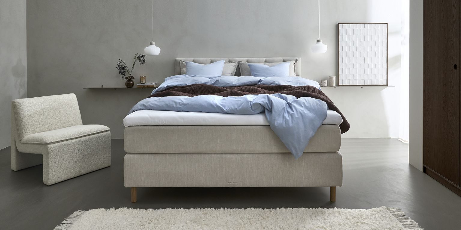 Sovrum med beige kontinentalsäng, vit fåtölj och annan dekoration