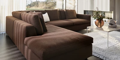 Brun schäslongsoffa i vardagsrum med vitt matta och soffbord