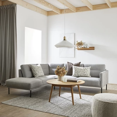 Mysigt vardagsrum med grå soffa, soffbord, hylla på väggen och pendellampa.