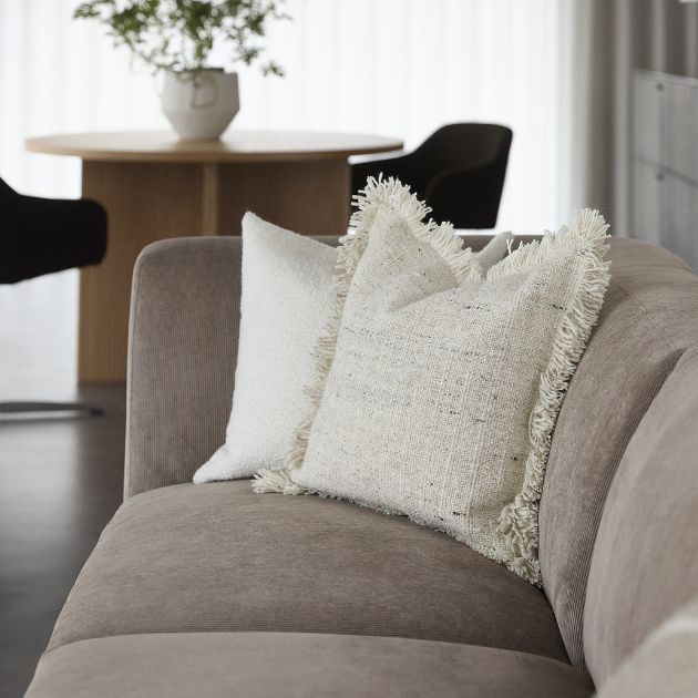 Närbild på soffa med ljusa kuddar och matbord i bakgrunden.