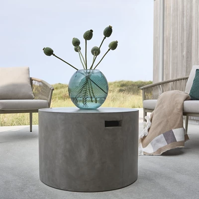 Runt loungebord i fibercement med en blå vas på toppen.
