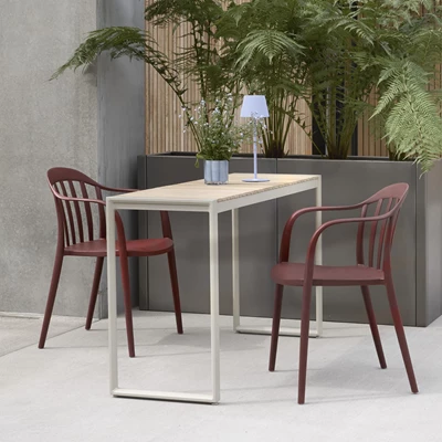 Smalt trädgårdsbord med träskiva tillsammans med två trädgårdsstolar i röd plast