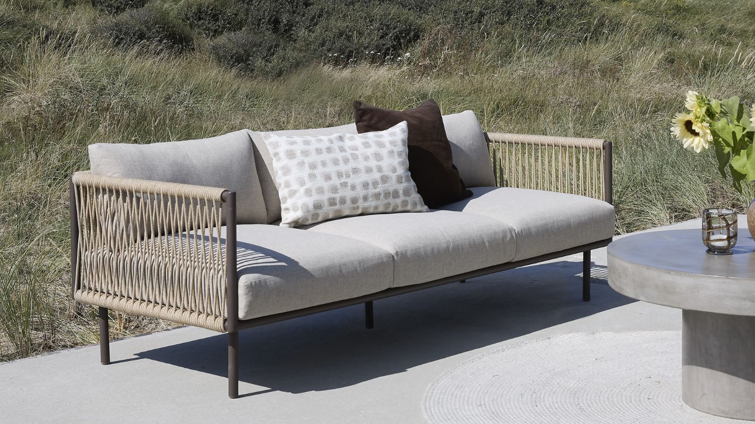 Loungesoffa med grå dynor och flätning på sidorna.