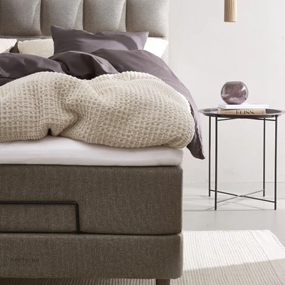 Närbild av ställbar säng bredvid runt sängbord med vas